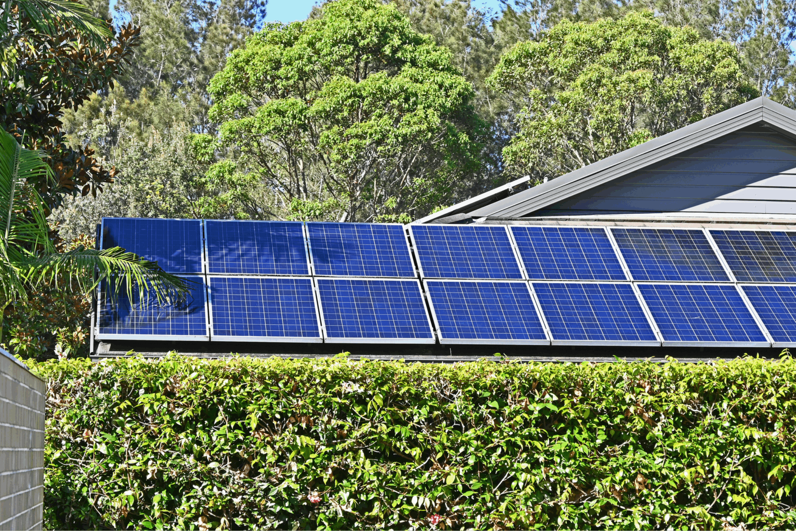 Solar electric panels on a house roof with a garden hedge in front of it